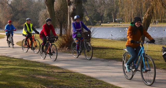 Several people in normal clothes, cycling along a path next to a river